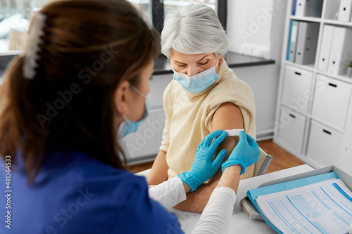 medicine, health and vaccination concept - doctor or nurse applying medical patch to vaccinated senior woman in mask at hospital