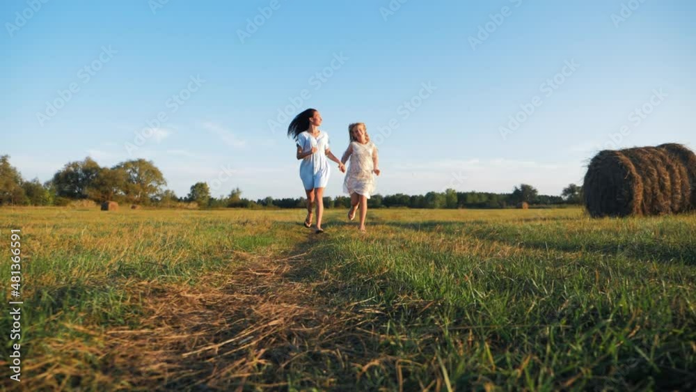 Friendly family. Mother and daughter holding hands at sunset running in the meadow. Happy mom and daughter walk holding hands towards the sunset in summer. Freedom happiness concept. Friendly family. Mother and daughter holding hands at sunset running in the meadow. Happy mom and daughter walk holding hands towards the sunset in summer. Freedom happiness concept.