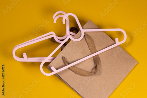 Creative sale and discount concept. Pink clothes hangers with shopping paper bag on yellow background top view flat lay.
