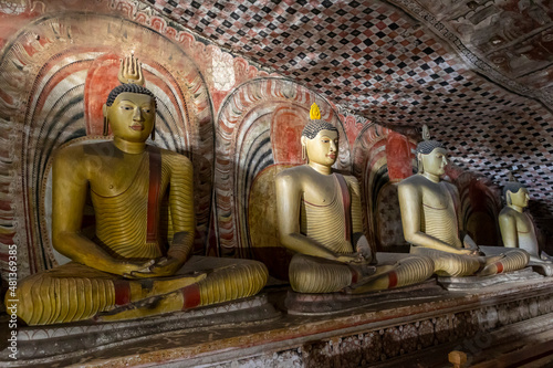 Sri Lanka. Dambulla Cave Temple. Buddha statues sitting in a row, illuminated by lamps from below.