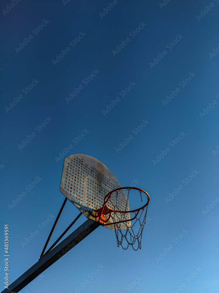 Orange basketball basket seen from the side with rusty metal net and blue sky in the background