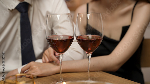 close up wine glasses and a Couple having romantic dinner at home in the background with dress up and suit