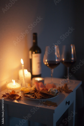 Candlelight date - two glasses of red wine and bottle of wine and appetizers with candles on the table