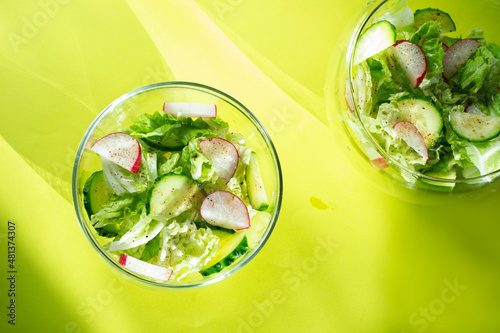 Salad with radish, cucumber and Chinese cabbage leaves. Fresh vegetable salad in a glass bowl on a green background. 