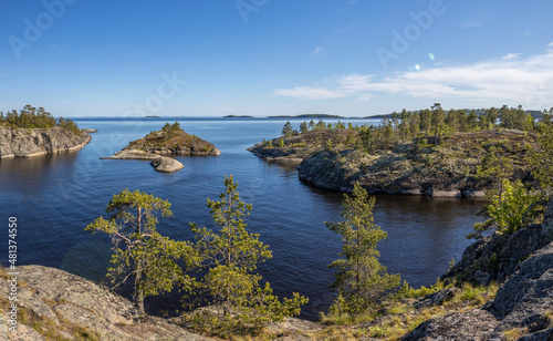 Landscape with a forest on stones over the lake. Sunny day at the lake. Reflection of the sky in the water. Pines on stones. The nature of the north.