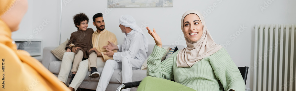 happy muslim woman talking to blurred mother near interracial family at home, banner.