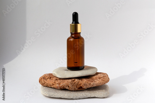 Tower from multi-colored stones with a brown oil bottle with a pipette on a white background. Natural podium with cosmetics