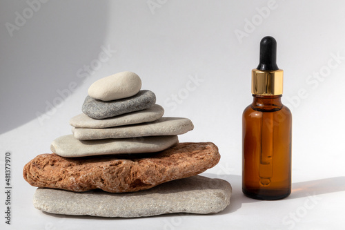 Tower from multi-colored stones with a brown oil bottle with a pipette on a white background. Natural podium with cosmetics