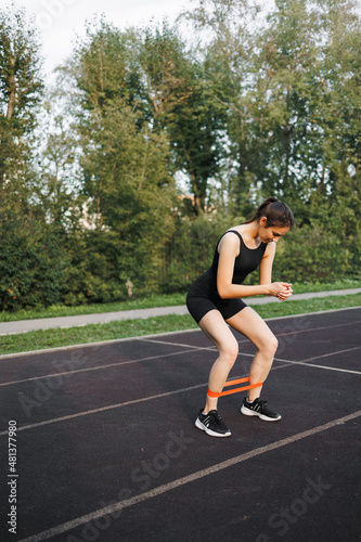 Fitness elastic band, elastic extensions for sports. Fitness with an outdoor expander. Close-up of a young athletic woman with a perfect body in sportswear performing exercises in a city park