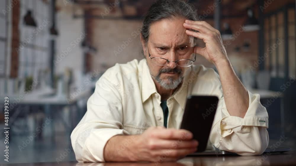 Mad unhappy man feeling annoyed using smart phone. Angry businessman having problem with mobile spam message. Male user frustrated by low battery or bad signal concept sitting at office desk. Mad unhappy man feeling annoyed using smart phone. Angry businessman having problem with mobile spam message. Male user frustrated by low battery or bad signal concept sitting at office desk.