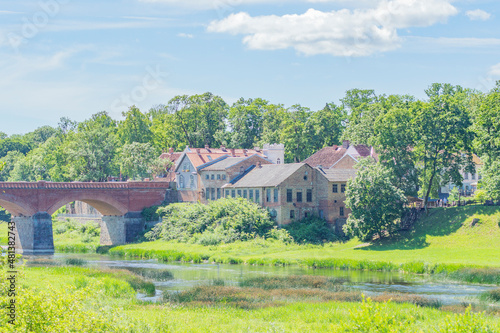 European summer cityscape: old buildings with tiled roofs, red brick bridge across the river, blue water and blue sky