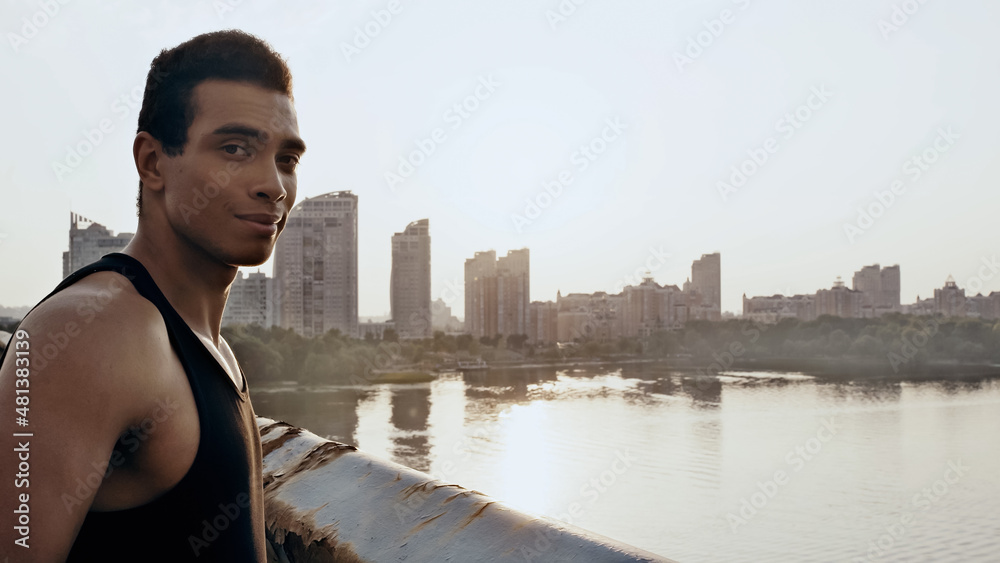 sportive bi-racial man looking at camera on city bridge over river.
