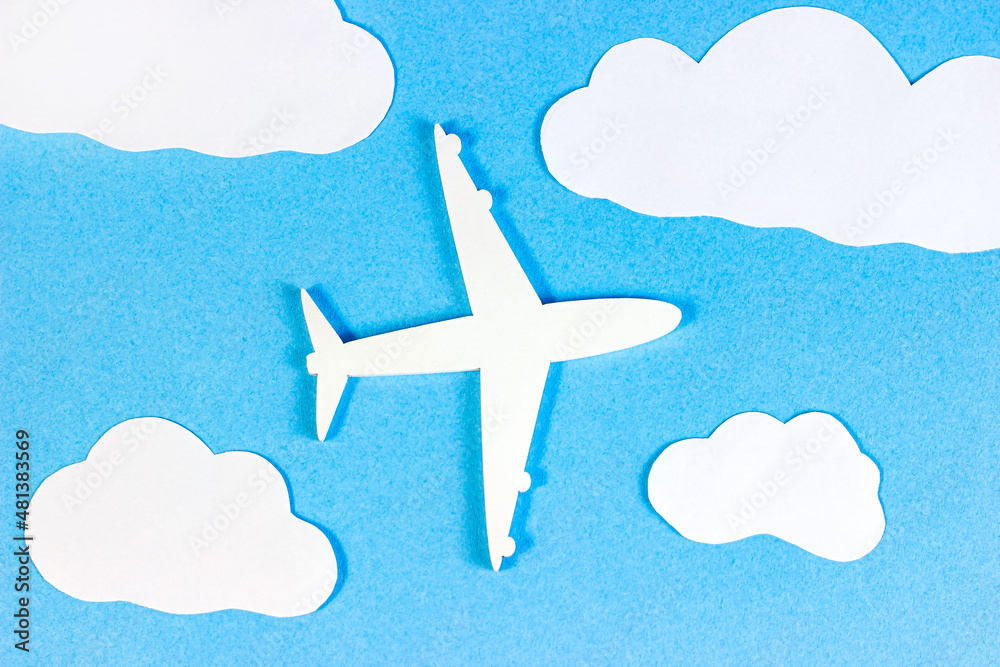 Fototapeta premium White plane model on light sky blue background with paper clouds top view flat lay.