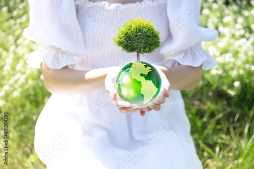 Earth Day or World Environment Day concept. Save our Planet, protect Green Nature, sustainable lifestyle and Climate literacy themes. Woman in white dress holding globe with growing tree in hands.