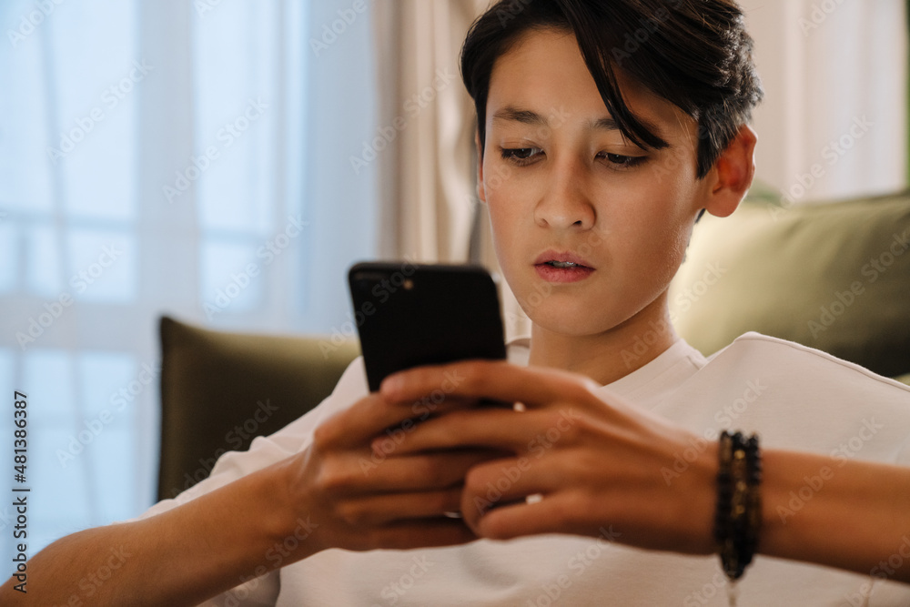 Asian boy using mobile phone while sitting on floor Asian boy using mobile phone while sitting on floor
