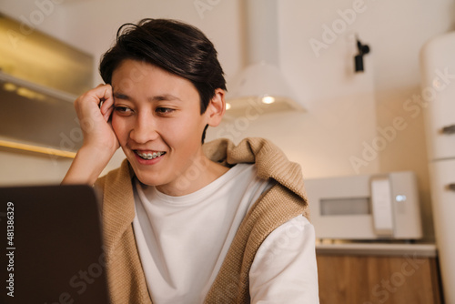 Asian boy working with laptop while sitting in kitchen