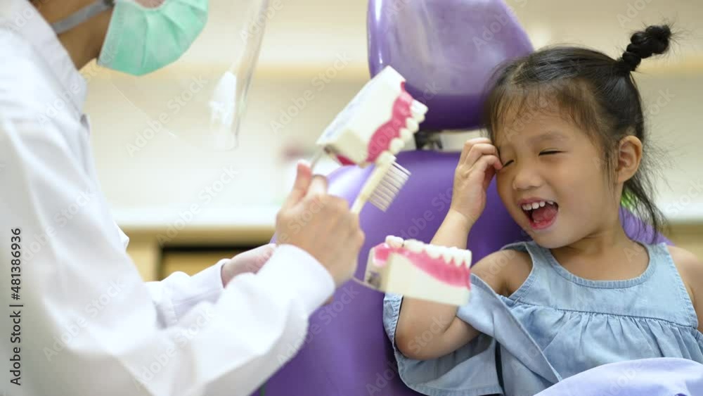 Asian female dentist wearing face mask and face shield teaching a little girl to brush tooth in dental clinic Asian female dentist wearing face mask and face shield teaching a little girl to brush tooth in dental clinic