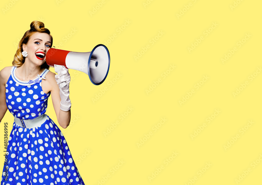 Portrait image of haired woman holding mega phone, shout advertising something. Girl in blue pin up style dress with mega phone loudspeaker. on yellow background. Beauty model in retro fashion concept - obrazy, fototapety, plakaty 
