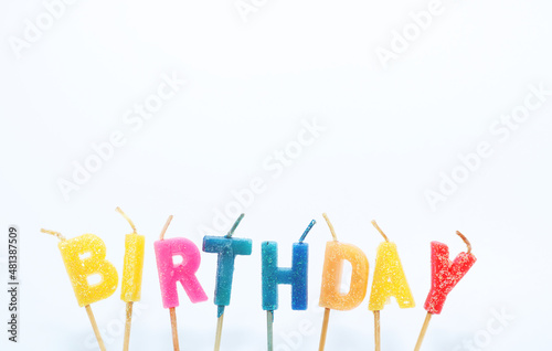 A candle with the word   BIRTHDAY  in bright colors against a white background.