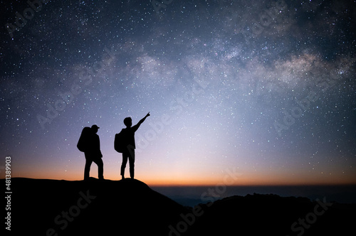 Silhouette of young couple traveler and backpacker standing and watched the star and milky way on top of the mountain. He enjoyed traveling and was successful when he reached the summit.