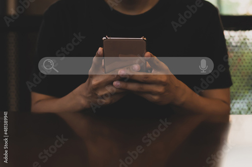 Young asian man wearing black t-shirt sitting on desk hand holding smartphone to Searching for information. Using Search Console with your website.