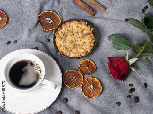 cup with black coffee, dried oranges, apple pie, cinnamon stick, coffee beans and red rose on brown background.
