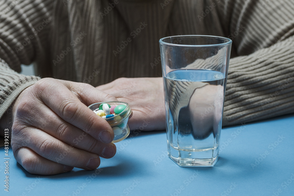 A man is sitting at a table and holding pills in his hands, there is a glass of water in front of him. A man is sitting at a table and holding pills in his hands, there is a glass of water in front of him.