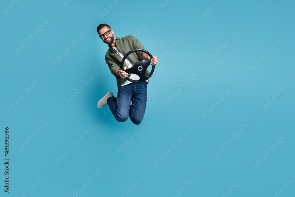 Full size photo of jumping man hold steering wheel traveling having fun isolated on blue color background Full size photo of jumping man hold steering wheel traveling having fun isolated on blue color background