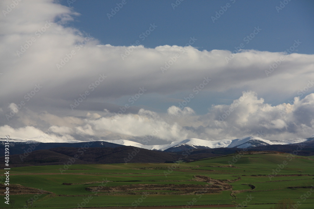 Montañas nevadas sobre cerros verdes en dia de cielo azul con nubes