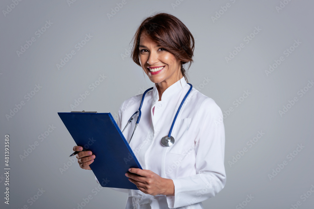 Female doctor standing at isolated grey background while holding clipboard in her hand Female doctor standing at isolated grey background while holding clipboard in her hand