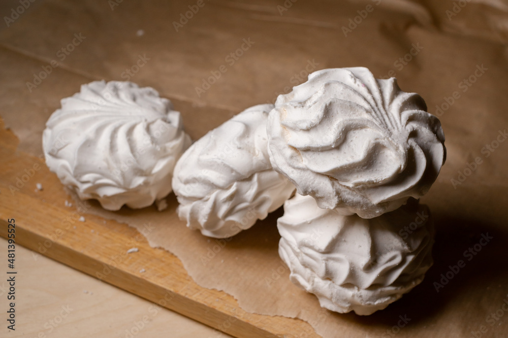 Obraz premium White marshmallows with vanilla flavor lie on a wooden cutting board on baking paper. Sweets for tea.