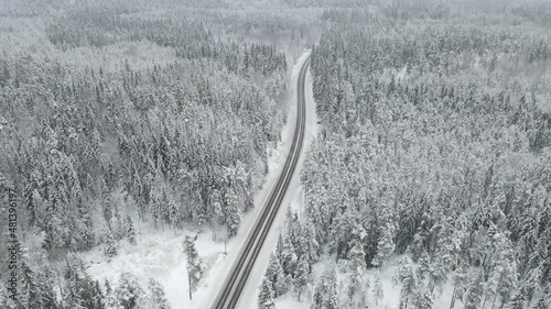 Aerial view from drone over snowy winter road with cars. Forest under hoarfrost in winter season. Highway in Finland.