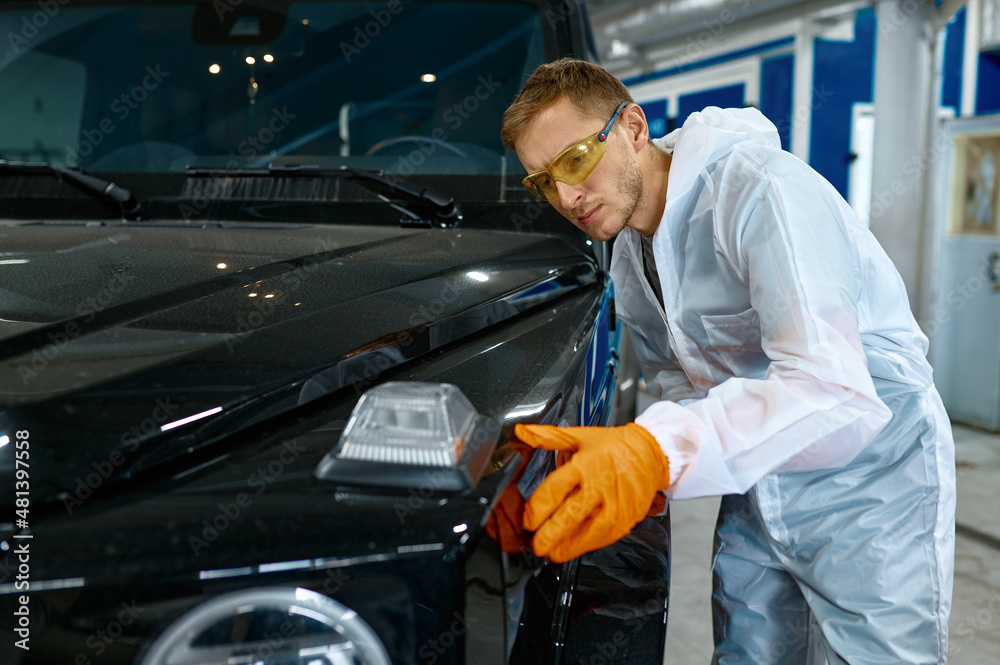 Serious repairman inspecting painting quality of vehicle