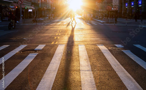 New York City - Person walking across the crosswalk on 14th Street and 5th Avenue in Manhattan with the sun shining in the background