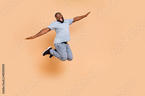 Full length body size view of attractive cheerful guy jumping flying having fun isolated over beige pastel color background © deagreez