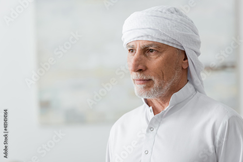 Fototapeta middle aged mislim man in white turban looking away at home.