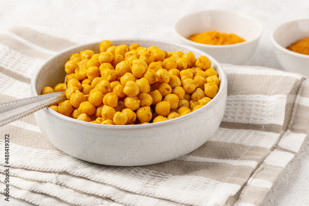 Indian traditional dish - roasted chickpeas with spices curry powder and turmeric in a light bowl on a striped napkin on white table. Close up Indian traditional dish - roasted chickpeas with spices curry powder and turmeric in a light bowl on a striped napkin on white table. Close up