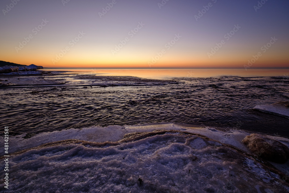 colorful beautiful sunset at sea in winter with snow on the beach