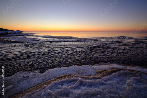 colorful beautiful sunset at sea in winter with snow on the beach