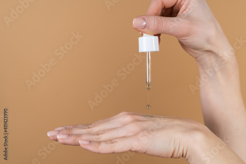 Close beauty photo of womans hands holds serum for youth and skin hydration  dropper with cosmetic oil  drop falling