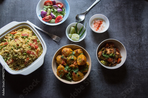 Indian lunch menu dum aloo or potato masala, pulao or vegetable fried rice and paneer or cottage cheese served with salad and condiments. Top view.