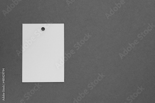 Brand label tag of white color made of cardboard for clothes with little hole in top part placed on left on dark gray background. Tag mock up. Copy space.
