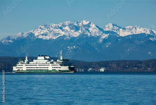 A ferry boat moves on Puget Sound with snow-capped Olympic mountains in the background on a winter day in Seattle, WA
