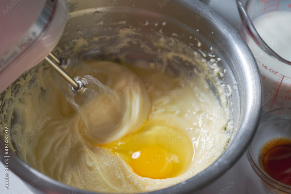 Making of a cake: Adding an egg and beating batter. Mixer beaters showing motion blur. Milk and vanilla in background. Making of a cake: Adding an egg and beating batter. Mixer beaters showing motion blur. Milk and vanilla in background.