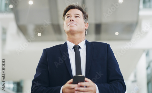 He's always thinking. Cropped shot of a mature businessman using a smartphone while walking through a modern office.