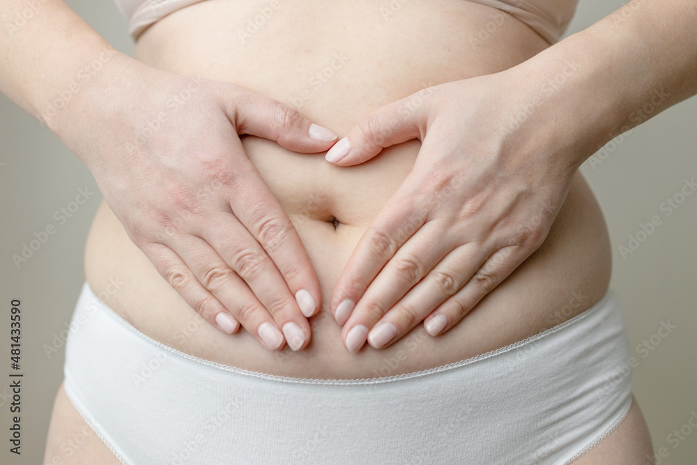 Closeup cropped of unrecognizable plus size woman in underwear holding hands on abdominal area forming heart shape around navel Closeup cropped of unrecognizable plus size woman in underwear holding hands on abdominal area forming heart shape around navel