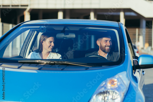 Male driving instructor and female driving school student sitting together in car smiling, learning to drive a car
