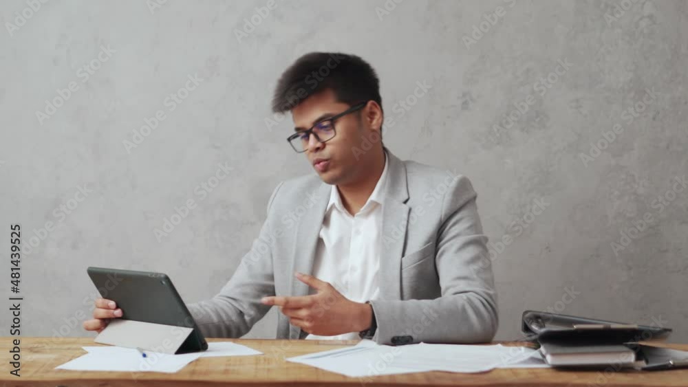 Emotional Indian businessman talking by video call on tablet in office Emotional Indian businessman talking by video call on tablet in office