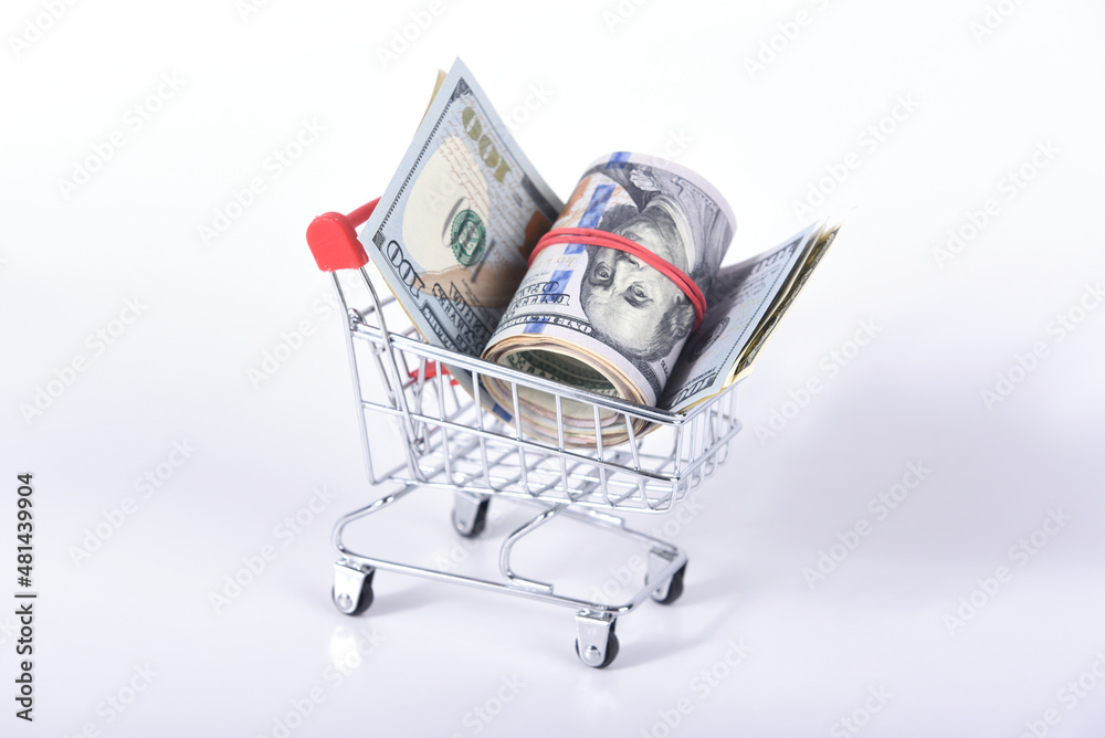 US dollar bills in loose and rolled into a ball in a rubber band in a mini supermarket cart on a white background