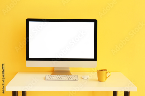 Modern computer and cup of tee near color wall